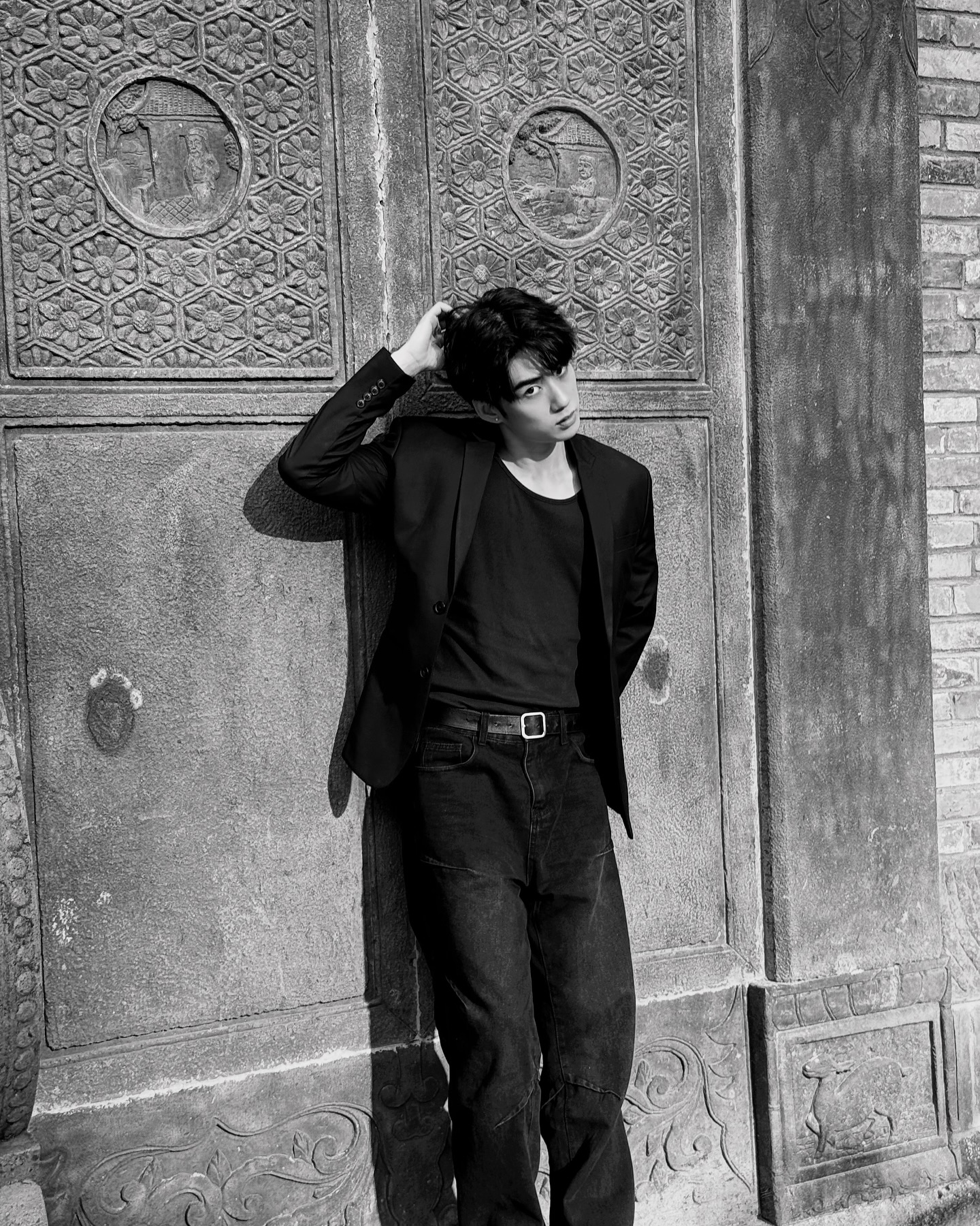 Black-and-white full-length portrait of YANG YAN by a carved wall
