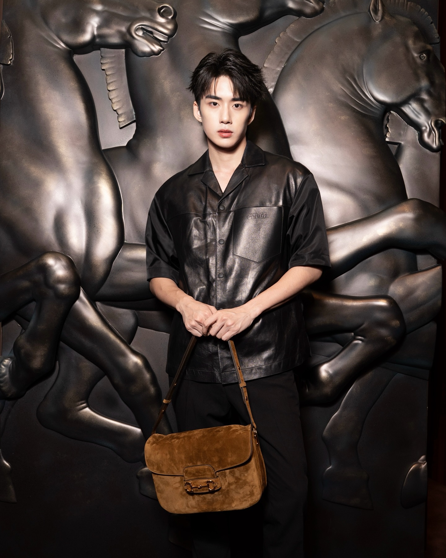 YANG YAN in a black leather shirt with a suede bag in front of a bronze horse relief