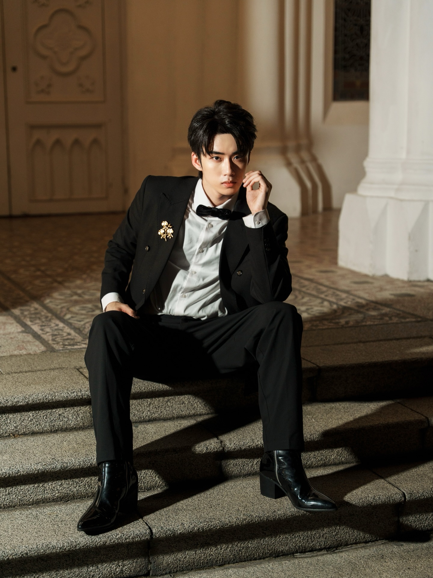 YANG YAN in a black tuxedo with a bow tie seated on stone steps at night