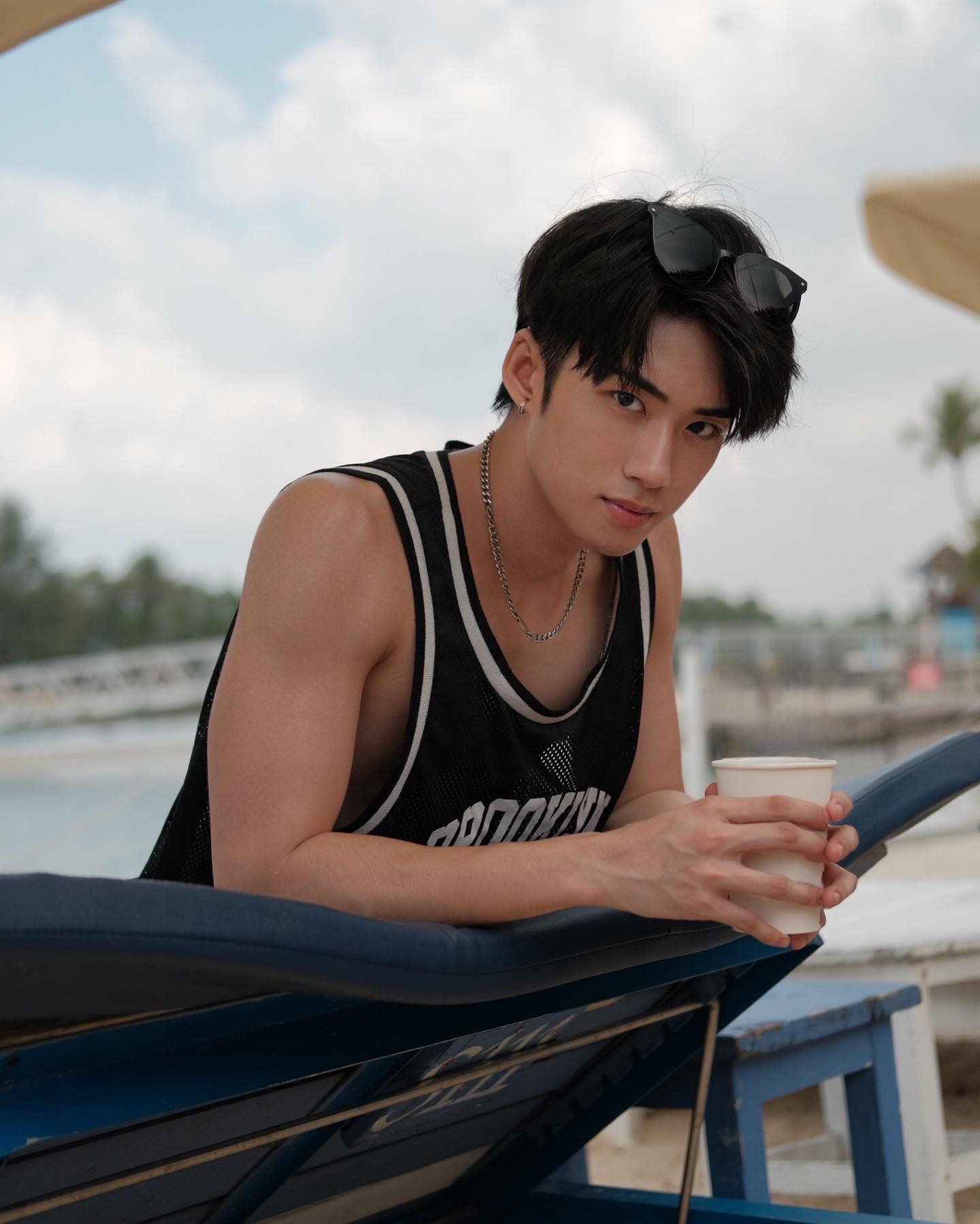 YANG YAN in a black mesh tank top holding a cup by the water