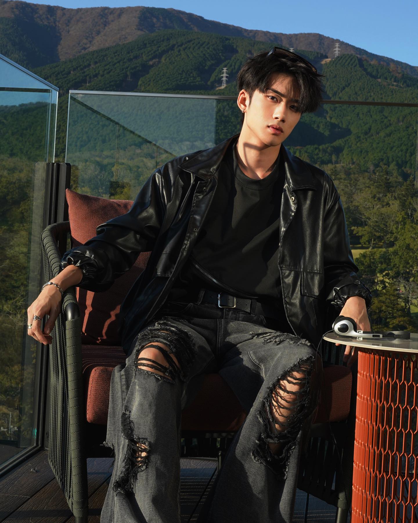 YANG YAN in a black leather jacket and ripped jeans on a terrace with mountains behind