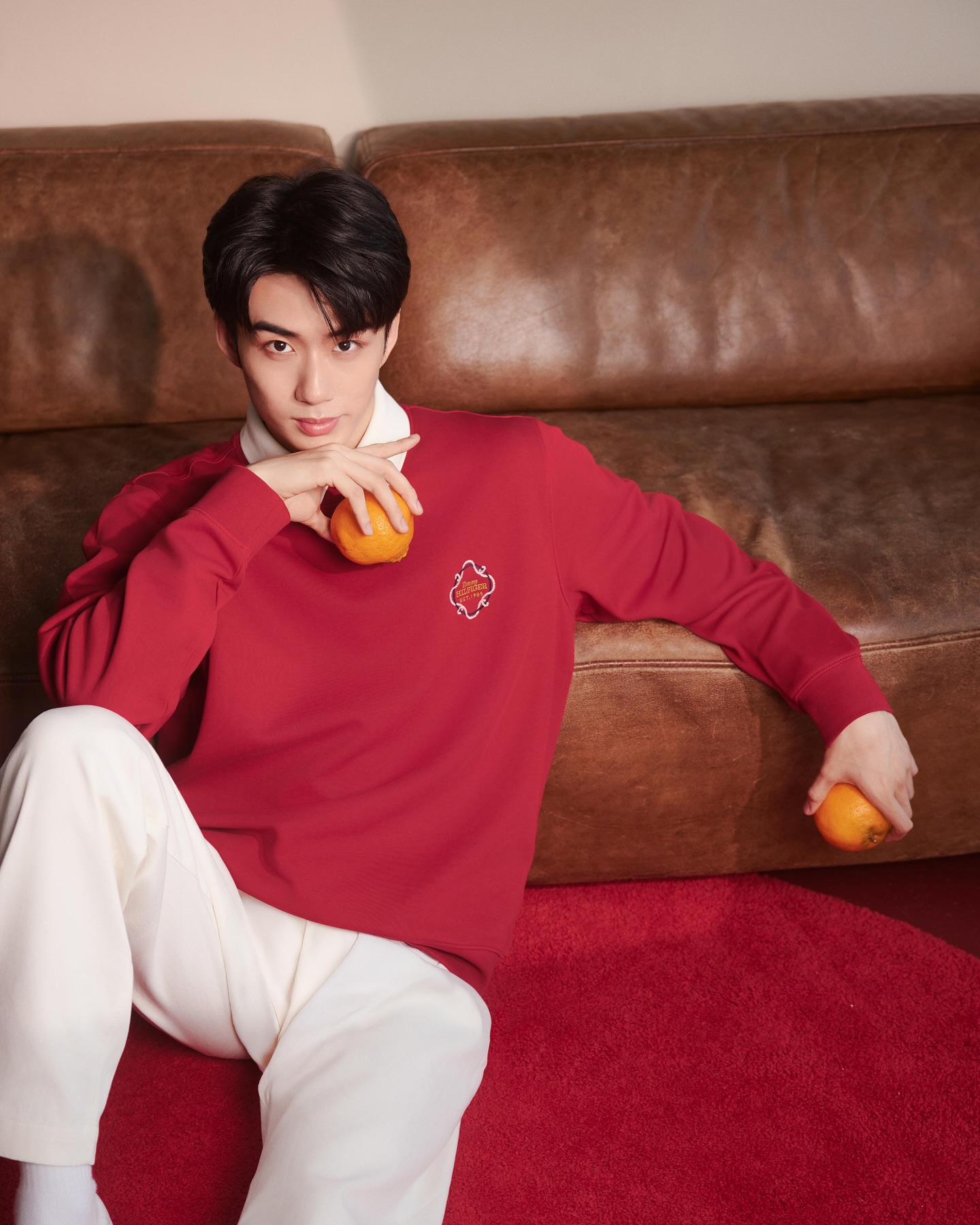 YANG YAN in a red sweatshirt holding oranges on a leather sofa