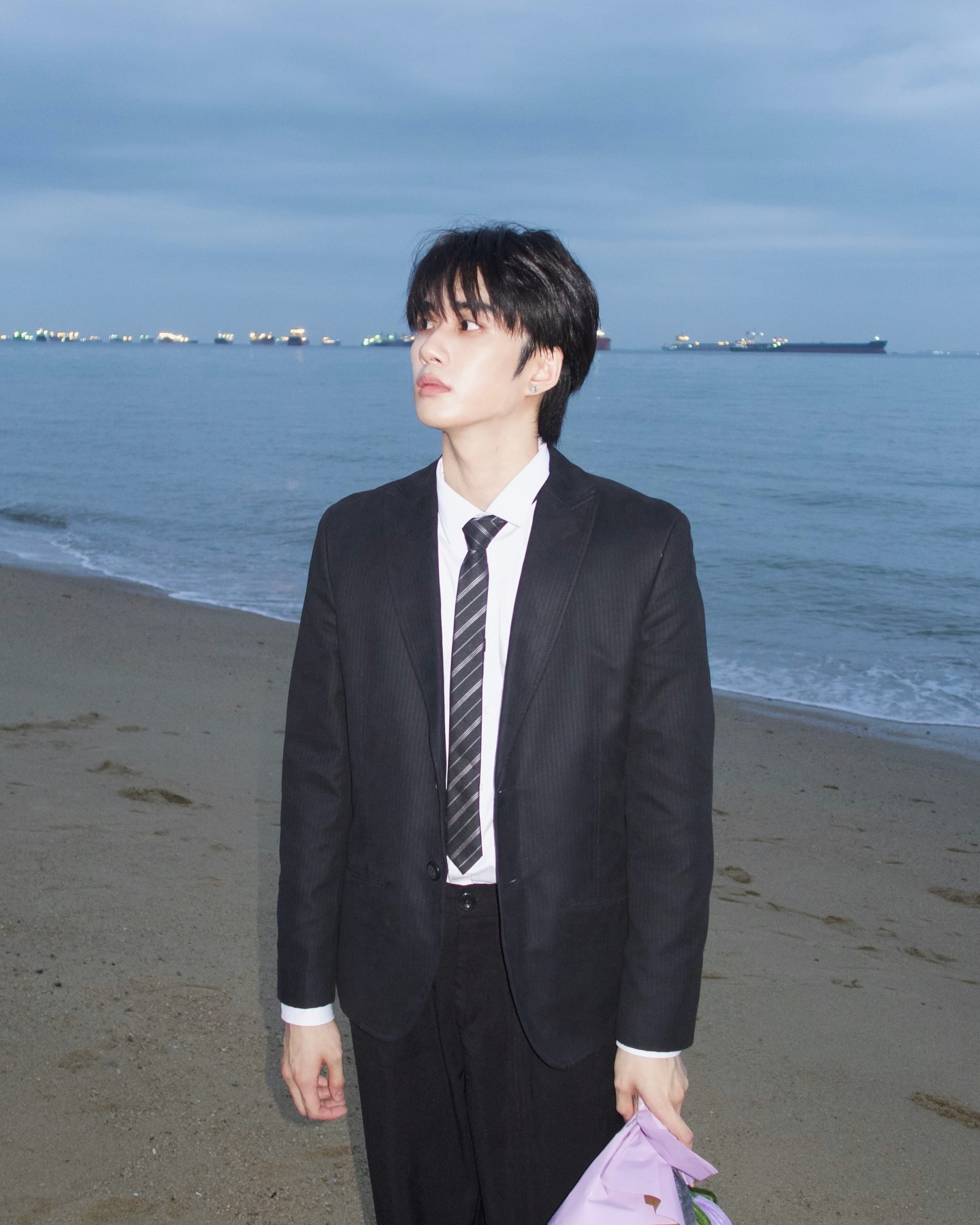 YANG YAN in a black suit and striped tie on a beach at dusk