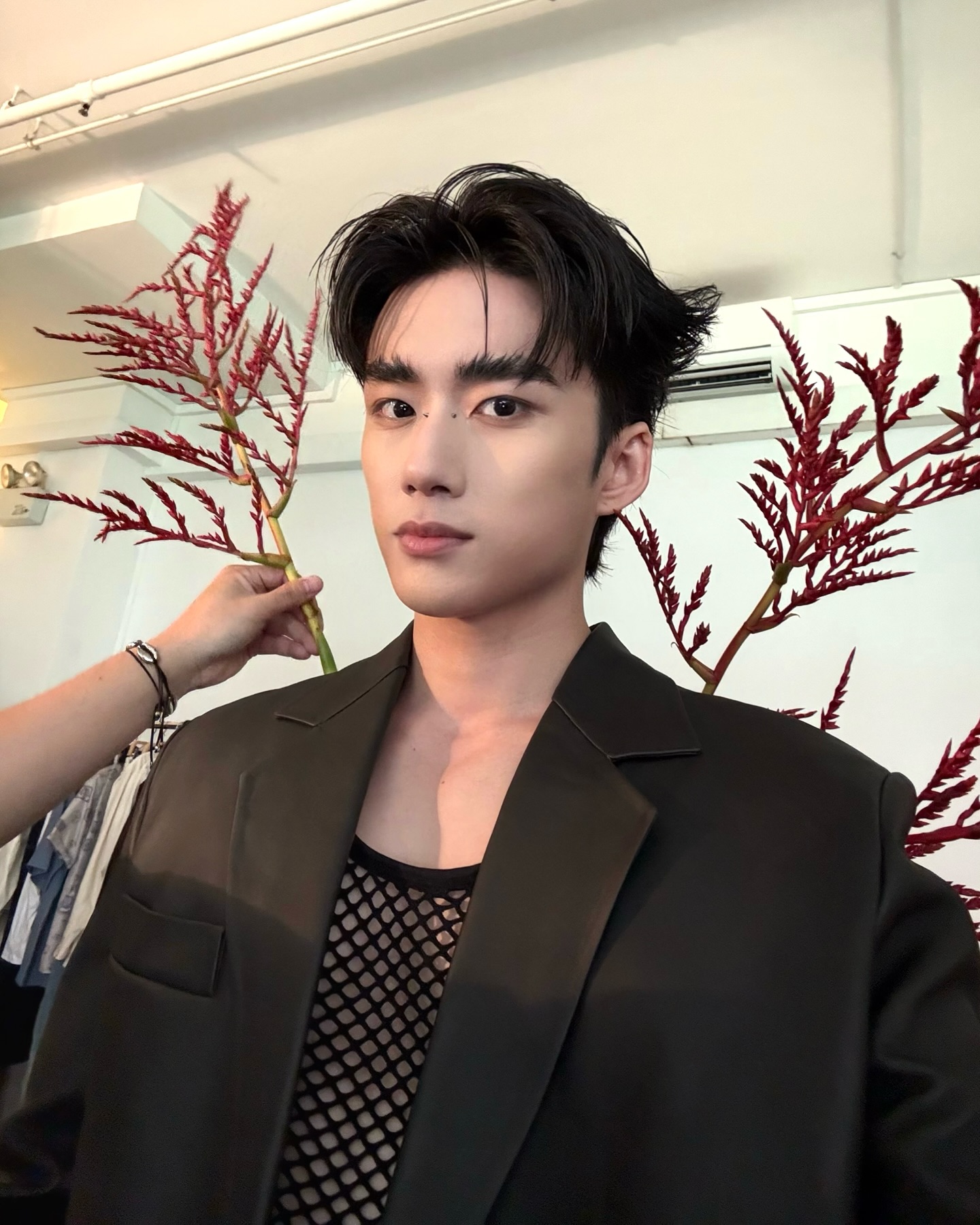 YANG YAN in a black blazer holding red flowers near a clothing rack