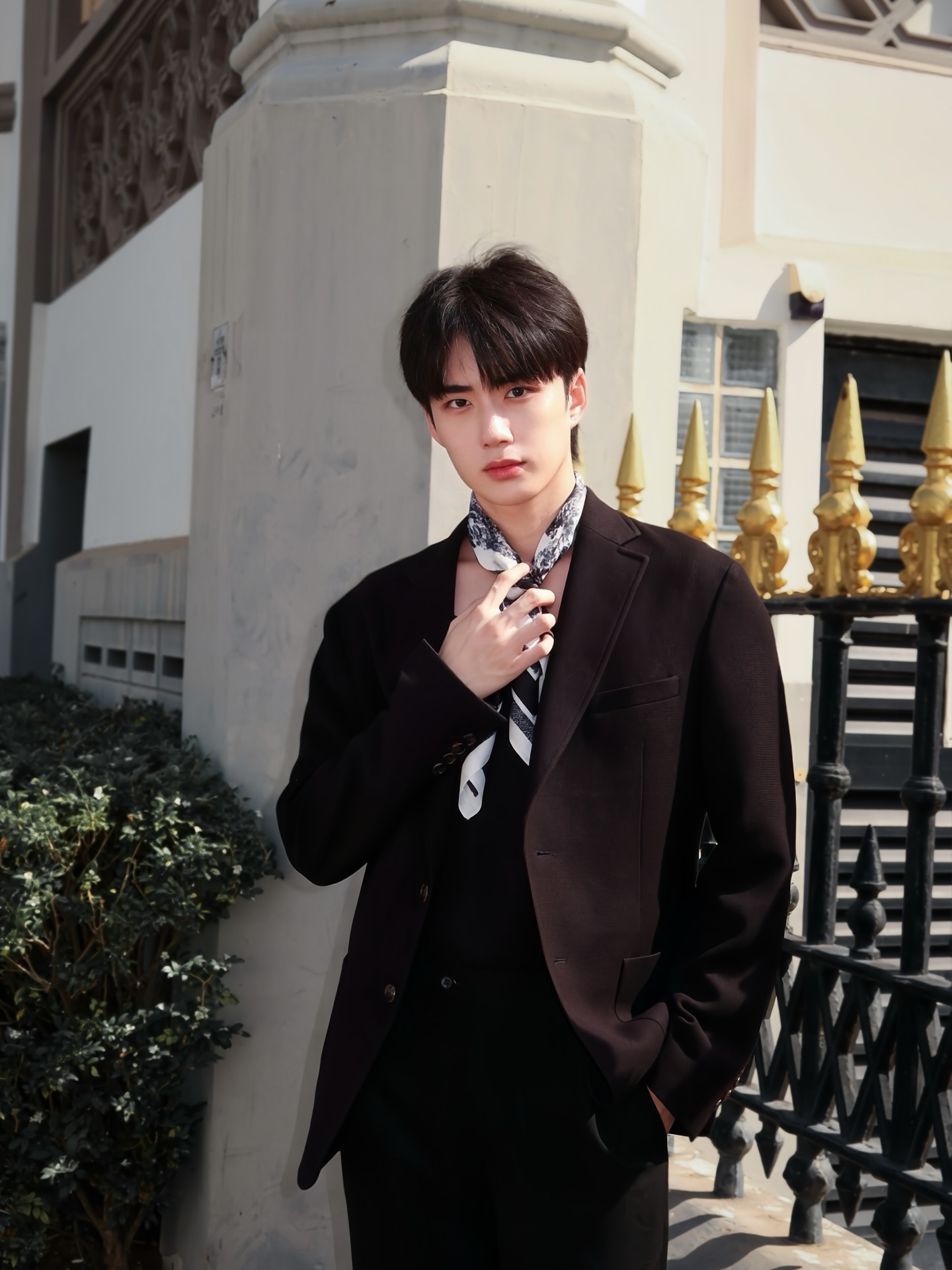 YANG YAN in a black suit with a silk scarf outside a white building with gold fencing