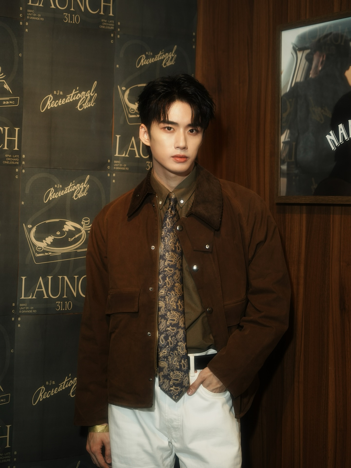 YANG YAN in a brown jacket and paisley tie at a launch event backdrop