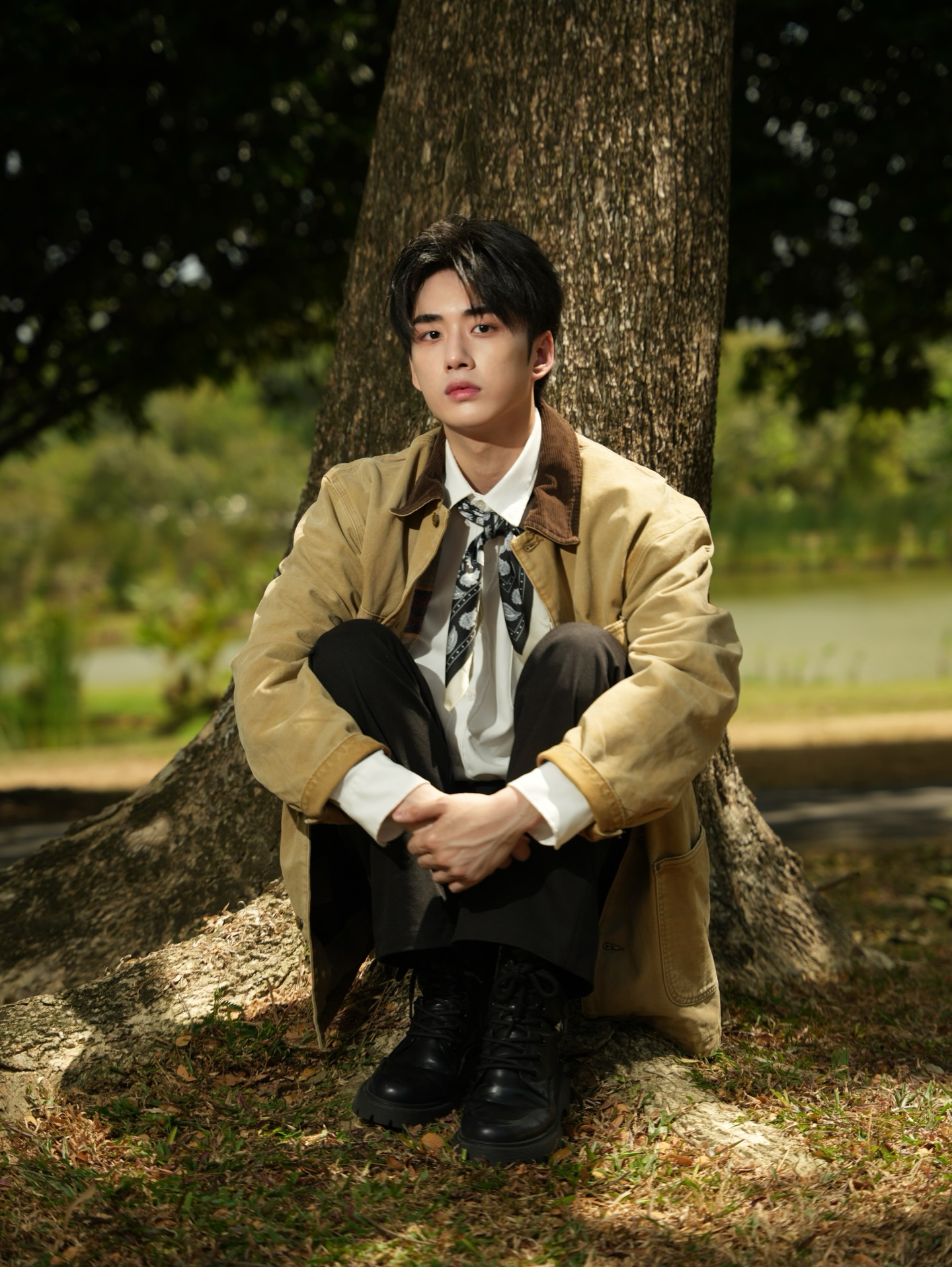 YANG YAN in a tan jacket sitting at the base of a tree