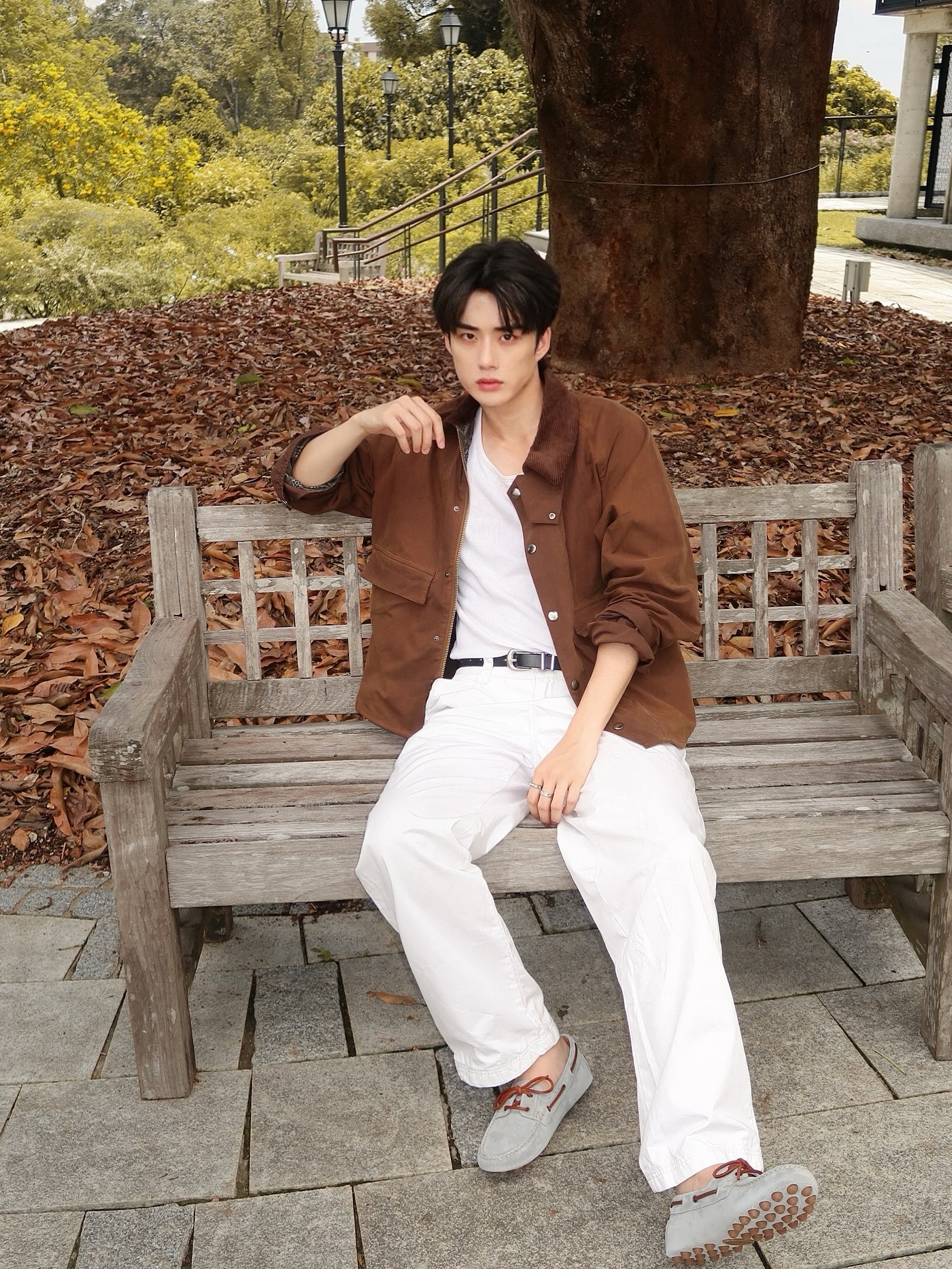 YANG YAN in a brown jacket and white trousers on a park bench