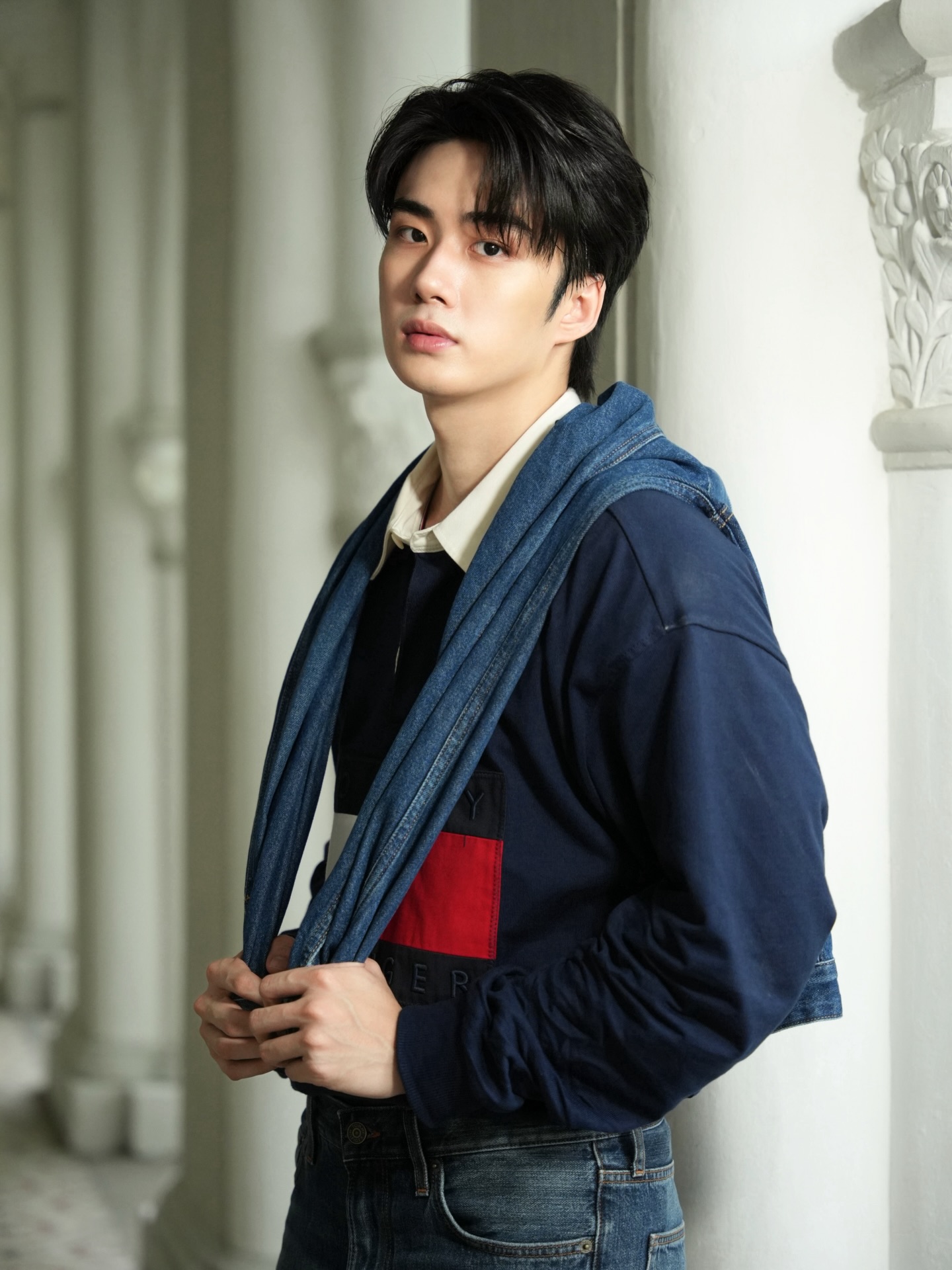 YANG YAN in a navy rugby shirt with a denim jacket draped over his shoulders