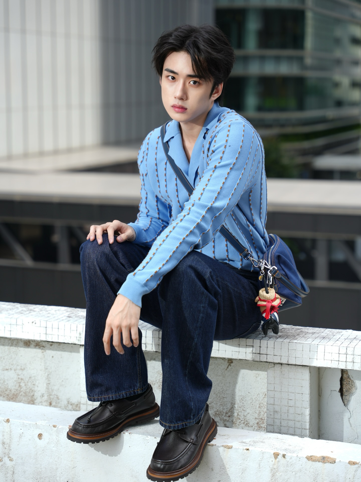 YANG YAN in a blue stitched knit and dark denim seated on a tiled bench