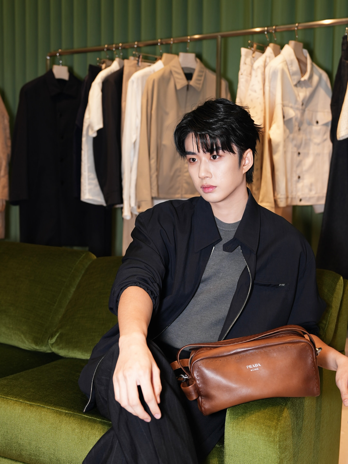 YANG YAN in a black jacket seated on a green sofa with a leather bag in a boutique